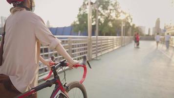 Junge Umweltliebhaberin im nackten hellen Blazer, die ihr Fahrrad vorwärts bewegt, Arbeiterin, die auf der Überführung über die Verkehrskreuzung schlendert, Hobby- und Gesundheitskonzept, männliche Kleidung, Tageslicht in Flammen video