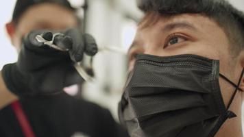 homem jovem asiático close-up rosto obter uma tesoura de corte de cabelo aparar o cabelo na barbearia usar máscara protetora preta. oportunidade de emprego, serviço de inicialização de negócios, pandemia covid-19 reabrir negócios video