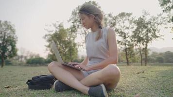 jeune étudiant aux cheveux blonds utilisant un ordinateur portable tout en se relaxant dans un parc public en plein air clair, étudiant à distance, apprenant en ligne ou travaillant avec Internet sans fil, technologie moderne, appareils pratiques video