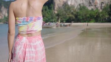Rear view of young pretty slim woman in casual island clothes walking on beautiful tropical beach. Relaxing walk on the sunny beach, thailand longtail boat, amazing, summer vacation, slow motion video