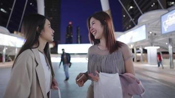 East asian female shopper joyfully walking talking together, a downtown shopping on a discount sale, black friday, a female shopper looking inside friend's shopping bag, female leisure and hobby video