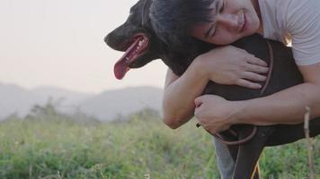 um momento engraçado de jovem asiático bonito abraçando seu cachorro em pé descansando no prado de primavera no fim de semana, atividade de lazer, um cão enérgico tentando escapar do abraço do dono, acariciando um cachorrinho video