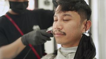 Asian male get hair cut. During quarantine lock down period, electric hair trimmer shaving blade, guy barber Corona virus Covid-19 re-open business world Pandemic, owner of small business start up video