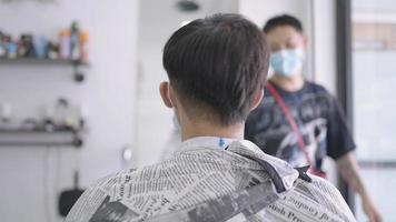 Aziatische jongeman wordt geknipt tijdens quarantainepandemie, wachtend op serviceweergave van achteren, heropening van de herenkapper, creatie van mannenhaarontwerper, klantenservicebaan, mannelijke hygiëne video