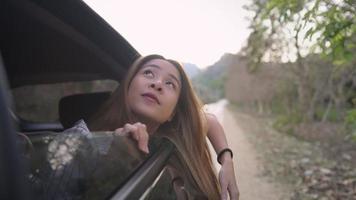 Young woman travelling with family in car, opens window look at clear sky, breathe fresh air of countryside, moves hand in the wind from tropical forests or asian rural area on side way, out of city video