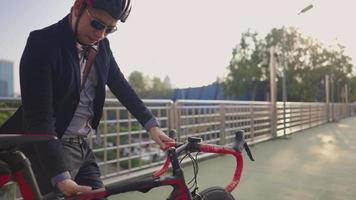 joven apuesto hombre relajante con ropa formal caminando al aire libre y llevando bicicleta en el hombro, cerca moderna del puente de la ciudad en el fondo, jinete masculino paseando y sosteniendo bicicleta, concepto ecológico
