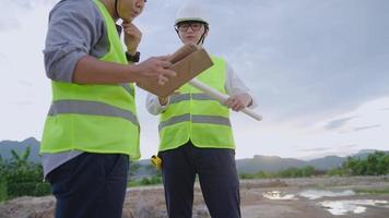 un'ingegneria professionale che accompagna un manager a camminare in una pozza di terra vuota, un moderno dispositivo tecnologico portatile, un team di costruzione e sviluppo, lavoro all'aperto, uniforme di sicurezza protettiva video