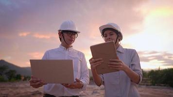 Asian Engineer and investor wear protective hardhat, using laptop and tablet talking on the project at outdoor site, colleague work environment, technology developer team, intern on the working site