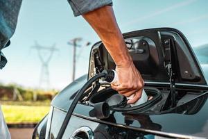 la mano humana sostiene la carga del automóvil eléctrico y se conecta al automóvil eléctrico foto