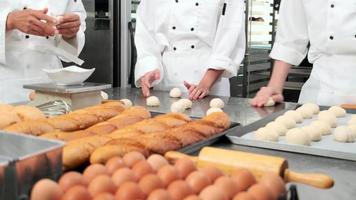 Close up of chefs' hand in white cook uniforms and aprons are kneading raw pastry dough, preparing bread, cakes, cakes, and fresh bakery food, baking in oven at stainless steel kitchen of restaurant. video