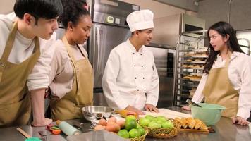 Cuisine course, senior male chef in cook uniform teaches young cooking class students to knead pastry dough and prepare ingredients for bakery foods, fruit pies in restaurant stainless steel kitchen. video