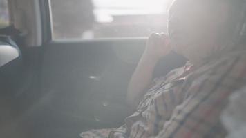 asiatische Seniorin, die mit der Hand am Kinn auf einem hinteren Beifahrersitz sitzt, über Lebens- und Gesundheitsprobleme nachdenkt oder andere Familienmitglieder vermisst, ältere Menschen, die sich im Familienauto blau fühlen