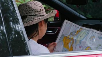 viajera asiática mirando un mapa buscando direcciones en el bosque mientras está sentada en un camión. los turistas viajan en el bosque de vacaciones en automóvil y verifican la ubicación del destino en el mapa de papel video