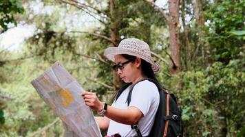 feliz joven turista con mochilas en un bosque tropical. una turista encuentra un sendero para caminar en un mapa mientras viaja por el bosque.
