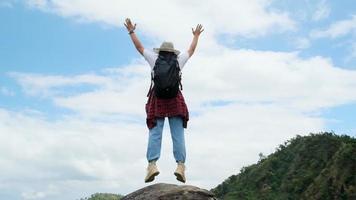 Backpacking female hiker stands on top of the mountain with raised arms and enjoying the view. journey and success concept video