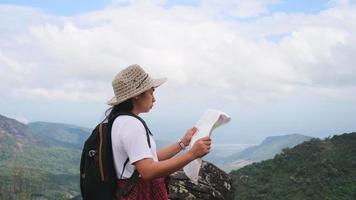 mujer hipster con mochila mirando un mapa en el fondo de las montañas. excursionista femenina descansando en la naturaleza y leyendo un mapa. video