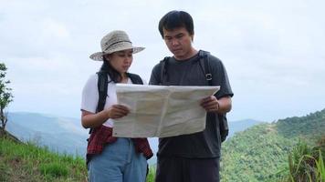 Man and woman travelers backpackers reading a map of summer vacation adventures in the mountains. Couple hikers searching looking for direction on map.