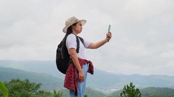 femme hipster dans un chapeau essaie d'obtenir un signal d'un téléphone portable dans les montagnes. une randonneuse dans un sac à dos se tient sur une montagne essayant d'attraper un signal de téléphone portable. video