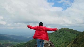 Young Asian hiker woman in a red raincoat standing on top of the mountain with raised arms and enjoying the view. journey and success concept video