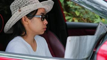 Asian female traveler looking at a map looking for directions in the forest while sitting in a car. Tourists travel in the forest on vacation by car and checking location of destination on paper map video