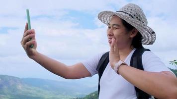 Hipster woman in hat relaxing in nature on vacation and making video call with smartphone on mountain background.