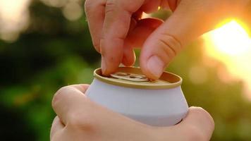 primer plano de manos abriendo latas de cerveza fría con fondo de naturaleza bokeh. video