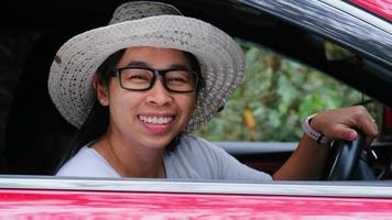 feliz viajante asiática senta-se em seu carro e acena antes de sua viagem. estilo de vida e viagens video