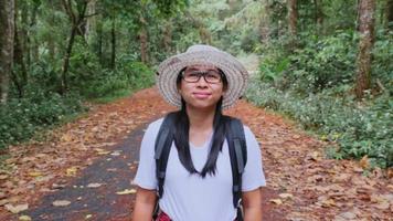 Female travelers enjoy the beauty of nature looking at the lush trees in the tropical forest. Hipster woman with a backpack walking on a road in the middle of nature. video
