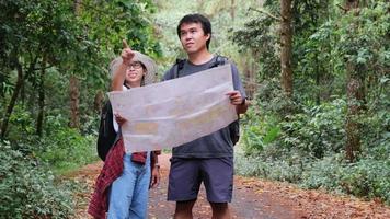 Asian tourist couple with backpacks in a tropical forest. Male and female tourists find walking directions on a map while traveling in the forest. video