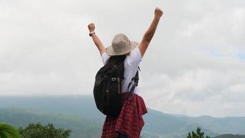 mochila alpinista feminina fica no topo da montanha com os braços levantados e apreciando a vista. conceito de viagem e sucesso