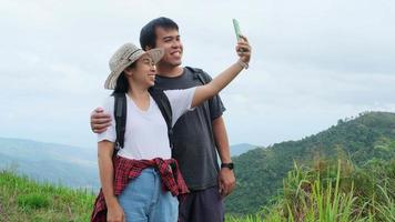 Man and woman travelers backpackers use mobile phones to take selfies on the mountain background. Hiking couple relaxing in nature on vacation.