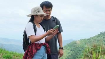 Man and woman travelers backpackers using mobile phone for navigation on a summer vacation adventure in the mountains. Two hikers searching for directions on smartphones.