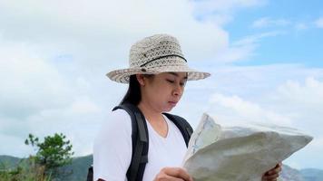 Hipster-Frau mit Rucksack, die eine Karte auf dem Hintergrund der Berge betrachtet. Wanderin, die sich in der Natur ausruht und eine Karte liest. video