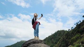 Hipster woman in hat relaxing in nature on vacation and taking selfie with smartphone on mountain background.