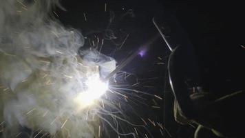 Nahhand des Metallschweißers, der mit einem Lichtbogenschweißgerät arbeitet, um Stahl im Werk mit Sicherheitsvorrichtungen zu schweißen. Funken und Blitze fliegen. video