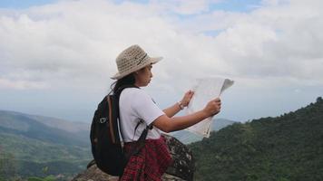 Hipster woman with backpack looking at a map on the background of mountains. Female hiker resting in nature and reading a map.