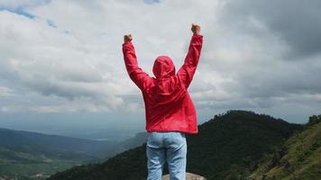 Young Asian hiker woman in a red raincoat standing on top of the mountain with raised arms and enjoying the view. journey and success concept video