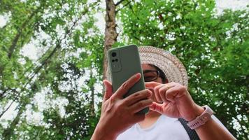 viajante feminina tira uma selfie em uma floresta tropical. mulher hipster com mochila usando telefone celular no fundo de árvores exuberantes na floresta.
