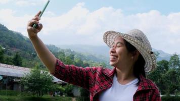 mujer hipster con sombrero relajándose en la naturaleza de vacaciones y tomando selfie con smartphone en el fondo de la montaña. video