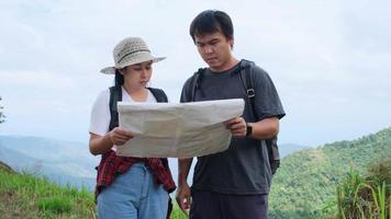 Man and woman travelers backpackers reading a map of summer vacation adventures in the mountains. Couple hikers searching looking for direction on map. video