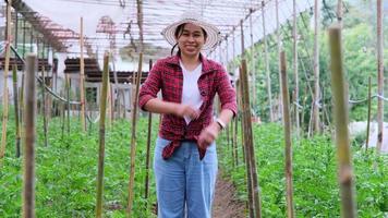 femme de jardinier asiatique heureuse debout avec les bras croisés et regardant la caméra dans le jardin. le propriétaire du jardin fleuri sourit à la caméra.