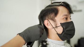 homem asiático cortando o cabelo na barbearia usa máscara protetora preta. oportunidade de trabalho barbeiro profissional. cuidados de saúde do homem, indústria de barbeiro durante a pandemia do vírus corona covid-19 reabrir negócios video