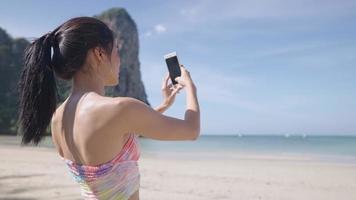 junge asiatische Dame, die einen Schnappschuss von der wunderschönen Aussicht auf das Meer macht, Sommerurlaubsreise, weibliche Touristen genießen den Inselstrand, nutzen das Smartphone, um Urlaubserinnerungen zu fotografieren, sonniger Meerblick am Strand video