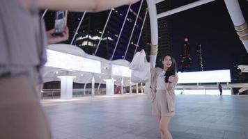 Pretty Asian woman and friend having fun together taking photos with smartphone, showing shopping bags, modern beautiful city architect landmark, hanging out on shopping on the weekend, travel Asia video