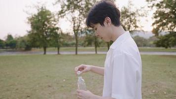 A young thirsty man drinking a pure water while walking inside green park on weekend, holding a reusable clean mineral bottle water, lifestyle healthcare concept, ecosystem caring, beauty sunset time