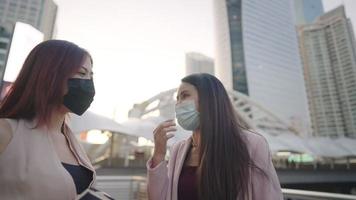 Two office female workers standing outside of building talking about heat weather during a day, female employee sweating after went out for lunch brake, showing a hands sign of rejection or unapproved video