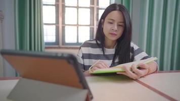 joven mujer asiática viendo usar tableta para la lección de clase de aprendizaje electrónico en línea, nueva vida normal durante el encierro, concentrada y enfocada en la tarea, matrícula de distancia, escuela en casa, tecnología inalámbrica