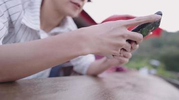 Side focus on hands movement of young female insanely playing game on smartphone while sitting on wooden bench against the natural mountain hill,  holding wireless device stay isolated from crowding video