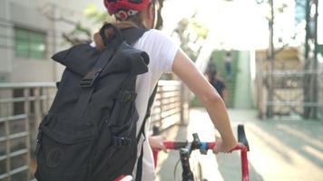 Back view closeup shot of teenage girl's back in casual dressing pushing bicycle up to the slope of city overpass during summer, young worker using bike to commute to workplace, saving cost, video