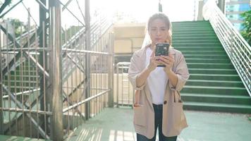 Attraktive Frau in Freizeitkleidung, die mit Smartphone in der Hand die schöne Stadtüberführung entlang geht, junge verlorene Studentin, die auf die Richtung blickt, die ihr Freund geschickt hat, lebt mit Smarts-Technologie video